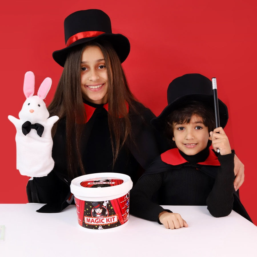 Two children in magician costumes with a magic kit against a red background